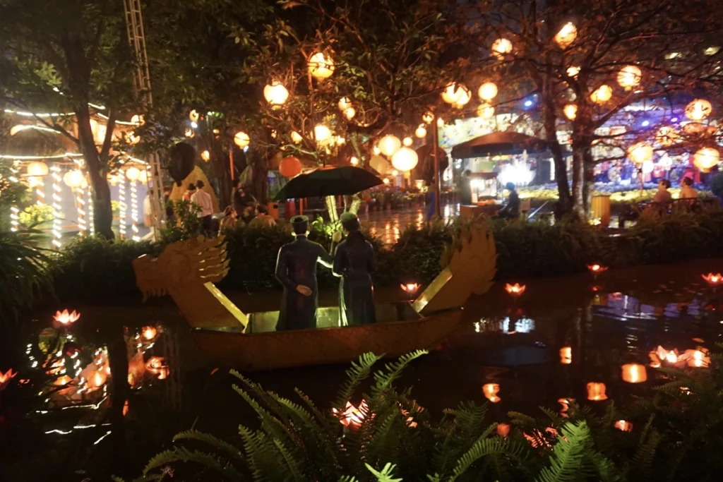 Illuminated dragon boat floating in a pond during a Hanoi night market, surrounded by glowing lanterns and lush greenery under the night sky.