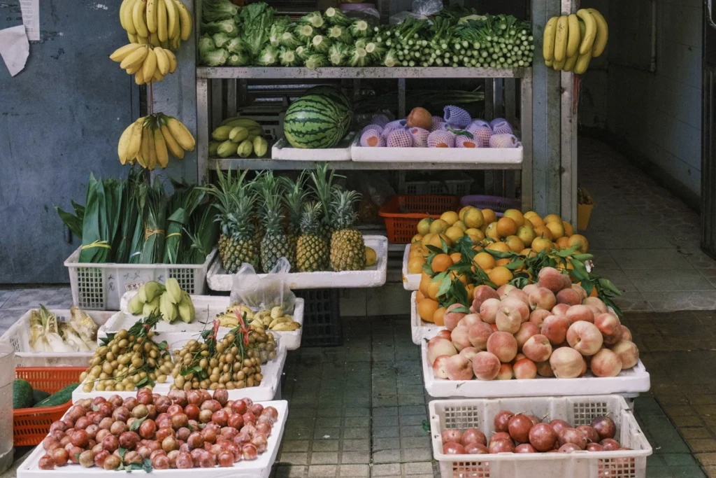 A street-side fruit stall displaying a colorful variety of produce, including bananas, pineapples, peaches, and pomelos, stacked in plastic crates. This affordable local market emphasizes how Vietnam offers fresh, budget-friendly food options for both locals and travelers.