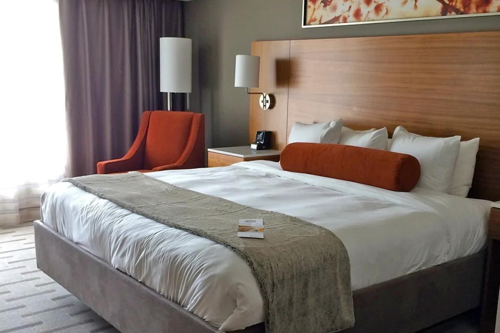 Modern hotel room with a cozy king-size bed, an orange armchair by the window, and elegant wood accents, perfect for a comfortable stay.