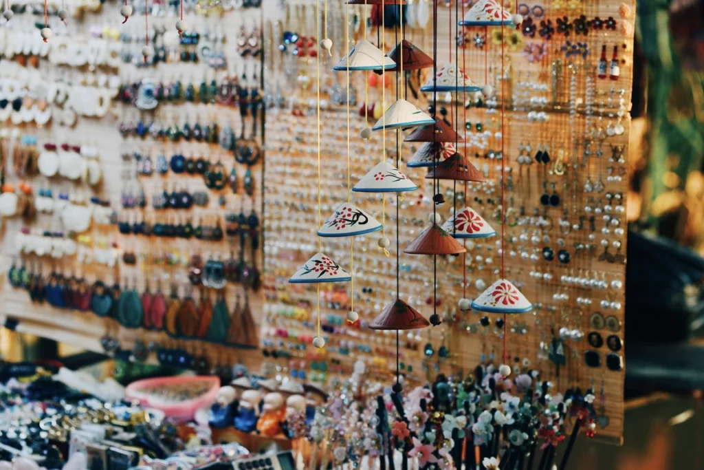 Colorful souvenirs including earrings, trinkets, and mini Vietnamese hats on display at a vibrant Hanoi night market stall.