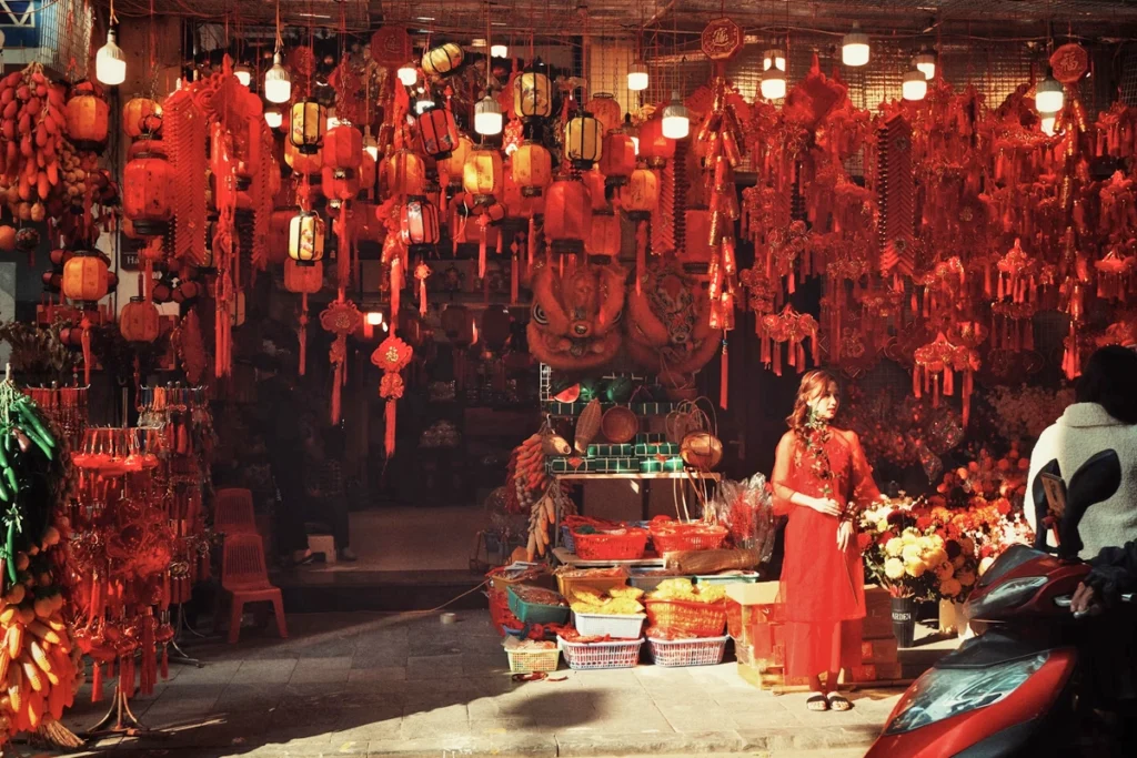Traditional Vietnamese shop filled with red decorations and lanterns, showcasing festive goods for sale with a woman in a red dress standing near the entrance.