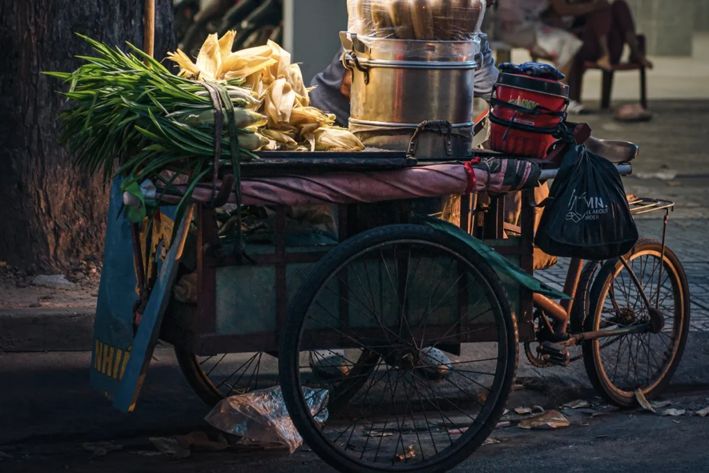 Vietnamese street food cart selling steamed corn and fresh greens, lit warmly in the evening, capturing the charm of Hanoi’s local food culture.