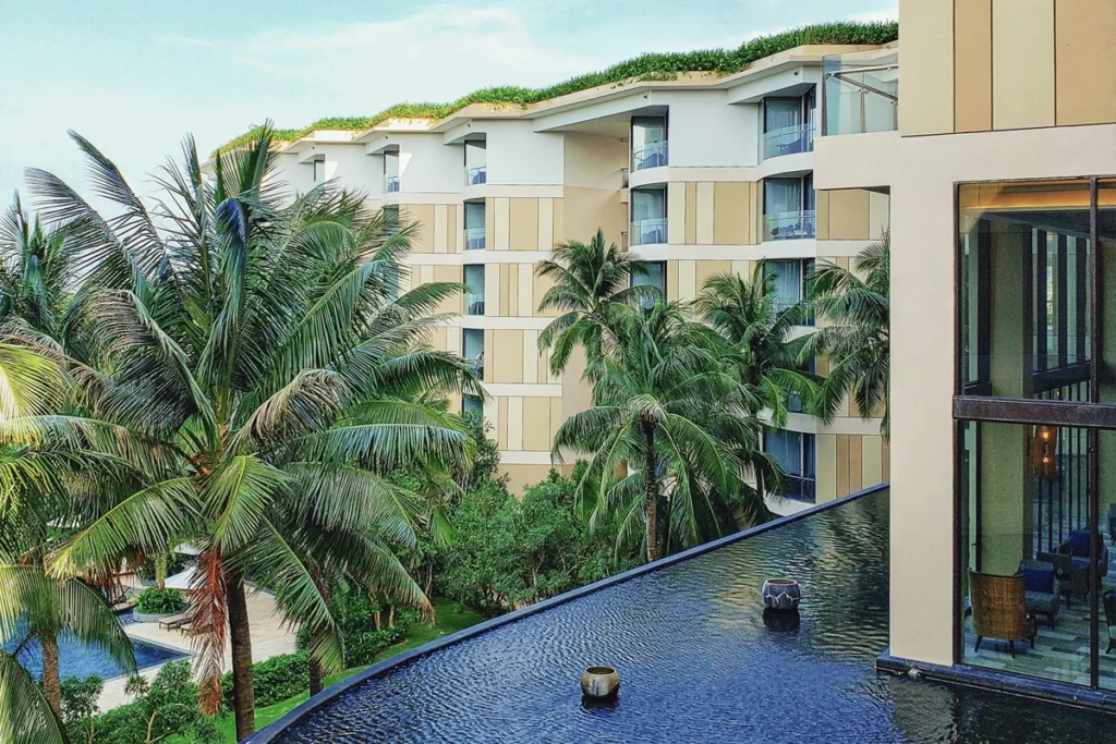 A luxury resort in Vietnam with modern architecture, palm trees, and an infinity pool reflecting the building's sleek design. The tropical setting, complete with lush greenery and private balconies, showcases Vietnam's blend of affordability and upscale experiences. This serene accommodation highlights how travelers can enjoy premium stays without breaking the bank.