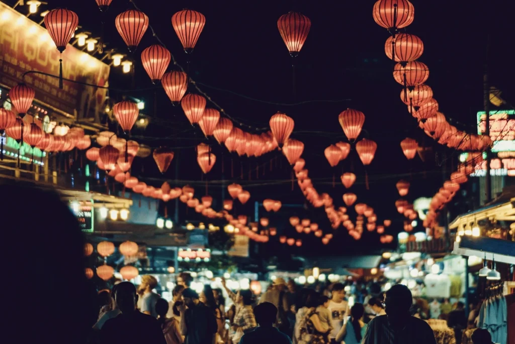 Red lanterns hanging across a bustling night market street in Hanoi, creating a festive and vibrant atmosphere under the dark sky.