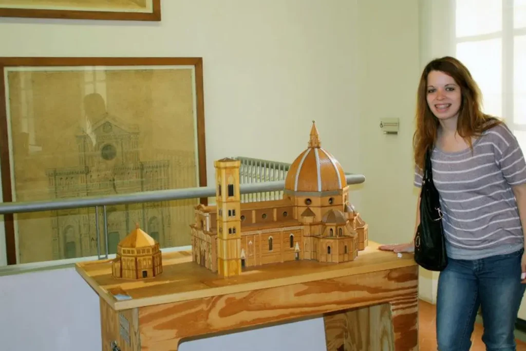 A woman standing next to a wooden model of the Florence Cathedral inside a museum. 